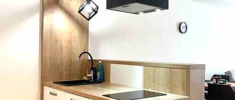 Une cuisine moderne avec un mur d’accent en bois, un luminaire suspendu noir et une cuisinière intégrée.