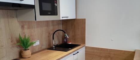 A modern kitchen with white cabinets, a black countertop, a built-in microwave, and a sink with a wooden backsplash.