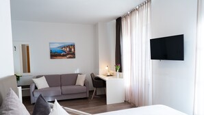 A modern hotel room with a bed, a desk, a sofa, and a TV. - Hotel La Fleur (Ueberlingen)