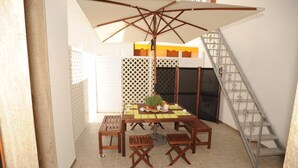 Ein kleiner Patio-Bereich mit einem Holztisch für vier Personen, einer Bank und einem großen Sonnenschirm.