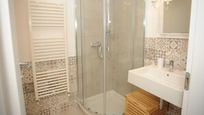 Ein modernes Badezimmer mit einer gläsernen Duschkabine, einem weißen Waschbecken und einer Wandfliese mit Muster.
