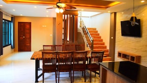 A modern dining area with a wooden table and chairs, a ceiling fan, and a staircase leading to an upper floor. - Poonsiri Private Pool Villa Aonang (Krabi)