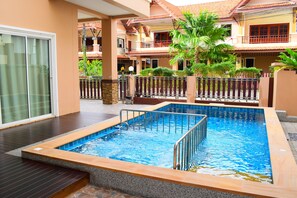 Une piscine dotée d’une terrasse en bois et d’une porte vitrée donnant sur un espace abrité.