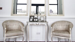 Une pièce comprenant deux fauteuils richement décorés, une petite table ornée d’objets décoratifs et trois grands miroirs, le tout surmonté d’un lustre.