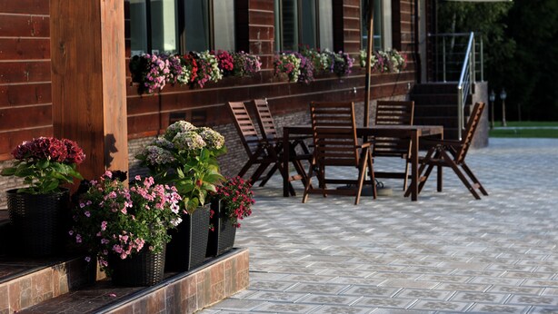 Une terrasse extérieure avec une table et des chaises en bois, un grand parasol et des jardinières disposées le long de la façade du bâtiment.