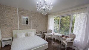 Une chambre à coucher avec un grand lit, un lustre, une petite table, deux chaises et une fenêtre avec des rideaux.