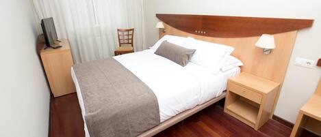A neatly arranged hotel room with a bed, a bedside table, a chair, a TV, and a window with curtains.