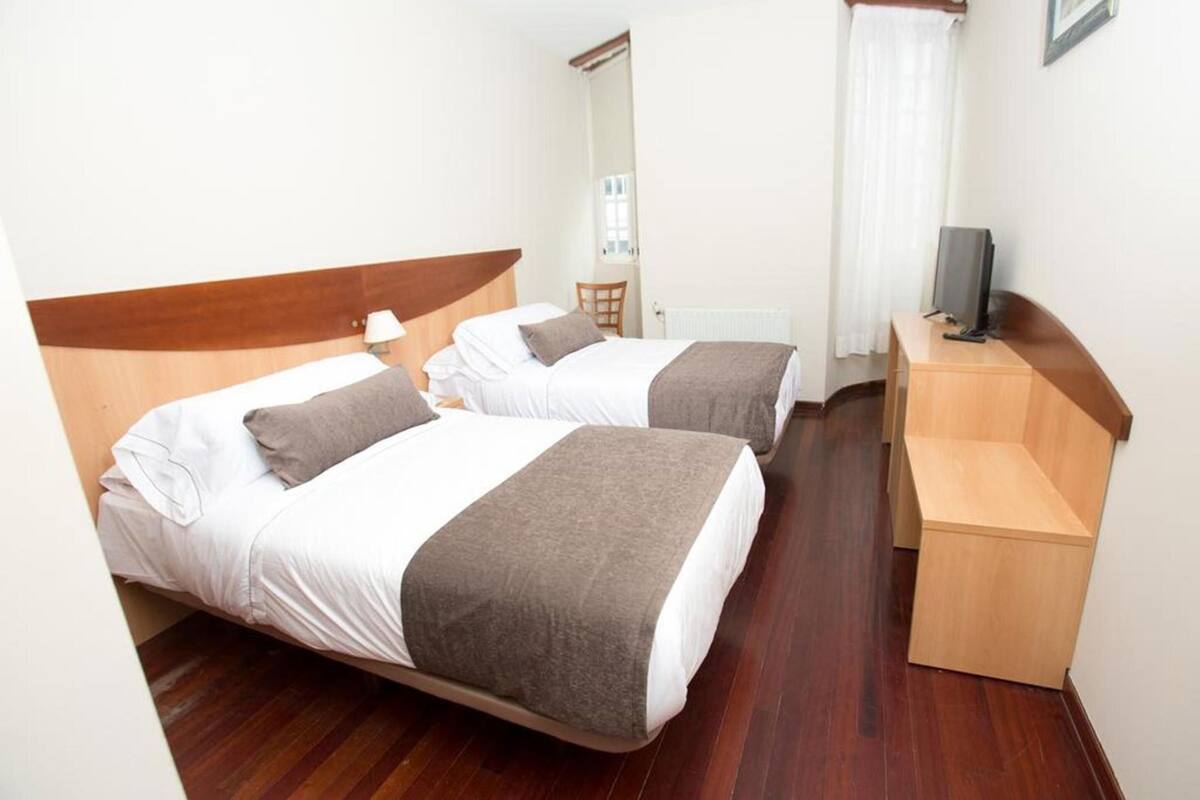 A hotel room with two beds, a desk, a chair, and a television.
