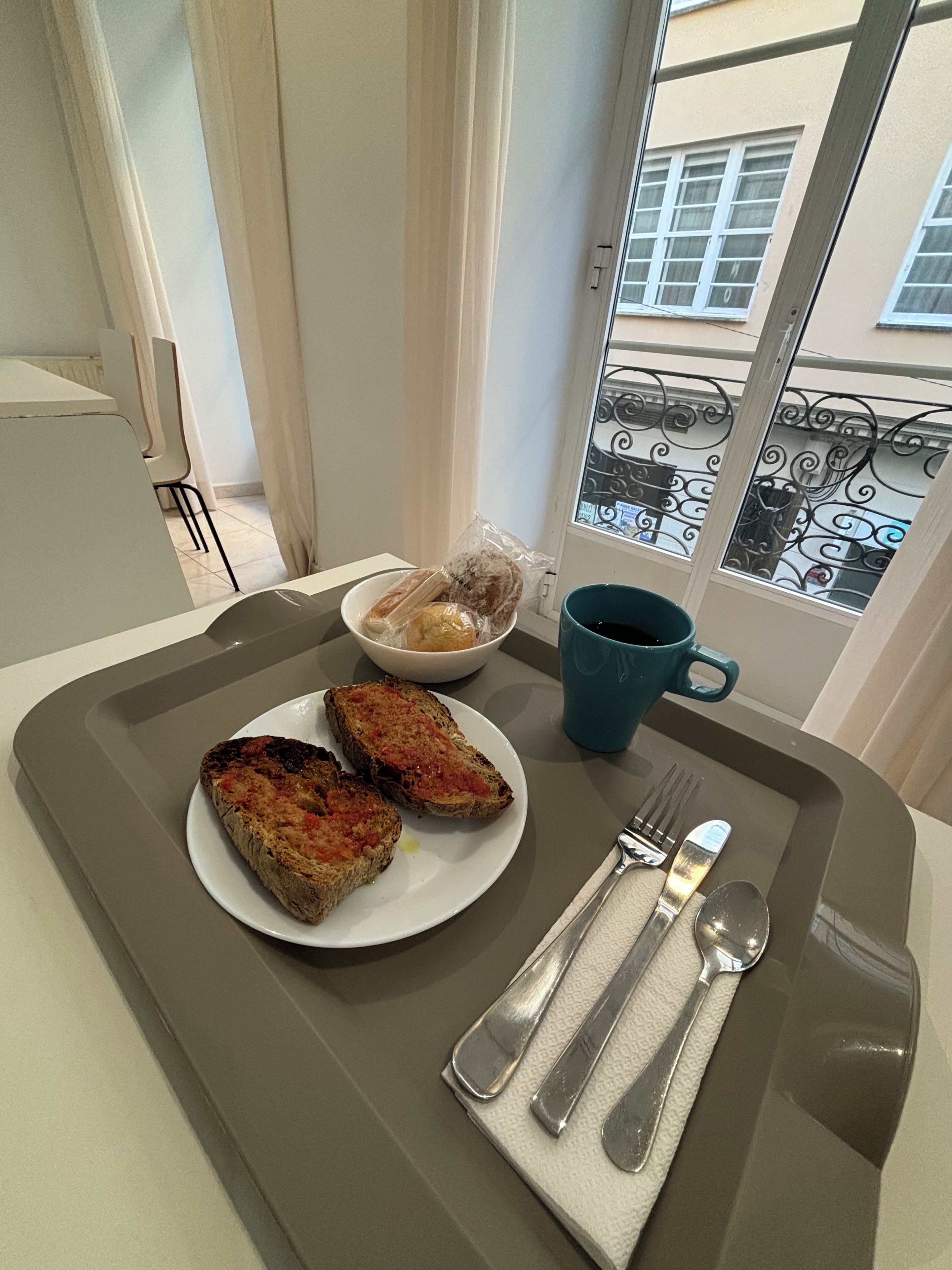 Un plateau de petit-déjeuner avec des toasts, un bol de viennoiseries et une tasse bleue posée sur un rebord de fenêtre.