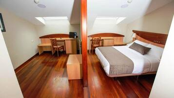 Quarto com cama, escrivaninha e cadeira, com piso de madeira e claraboia.