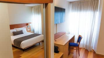 Una habitación de hotel con cama, escritorio, silla, televisor y cortinas.