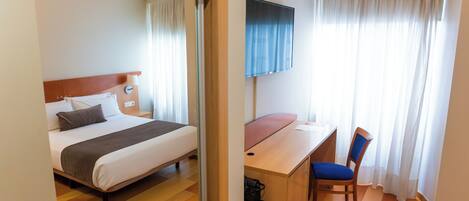 Una habitación de hotel con cama, escritorio, silla, televisor y cortinas.