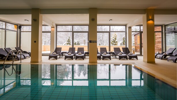 An indoor swimming pool with lounge chairs and large windows. - Hotel Trakoscan (Bednja)