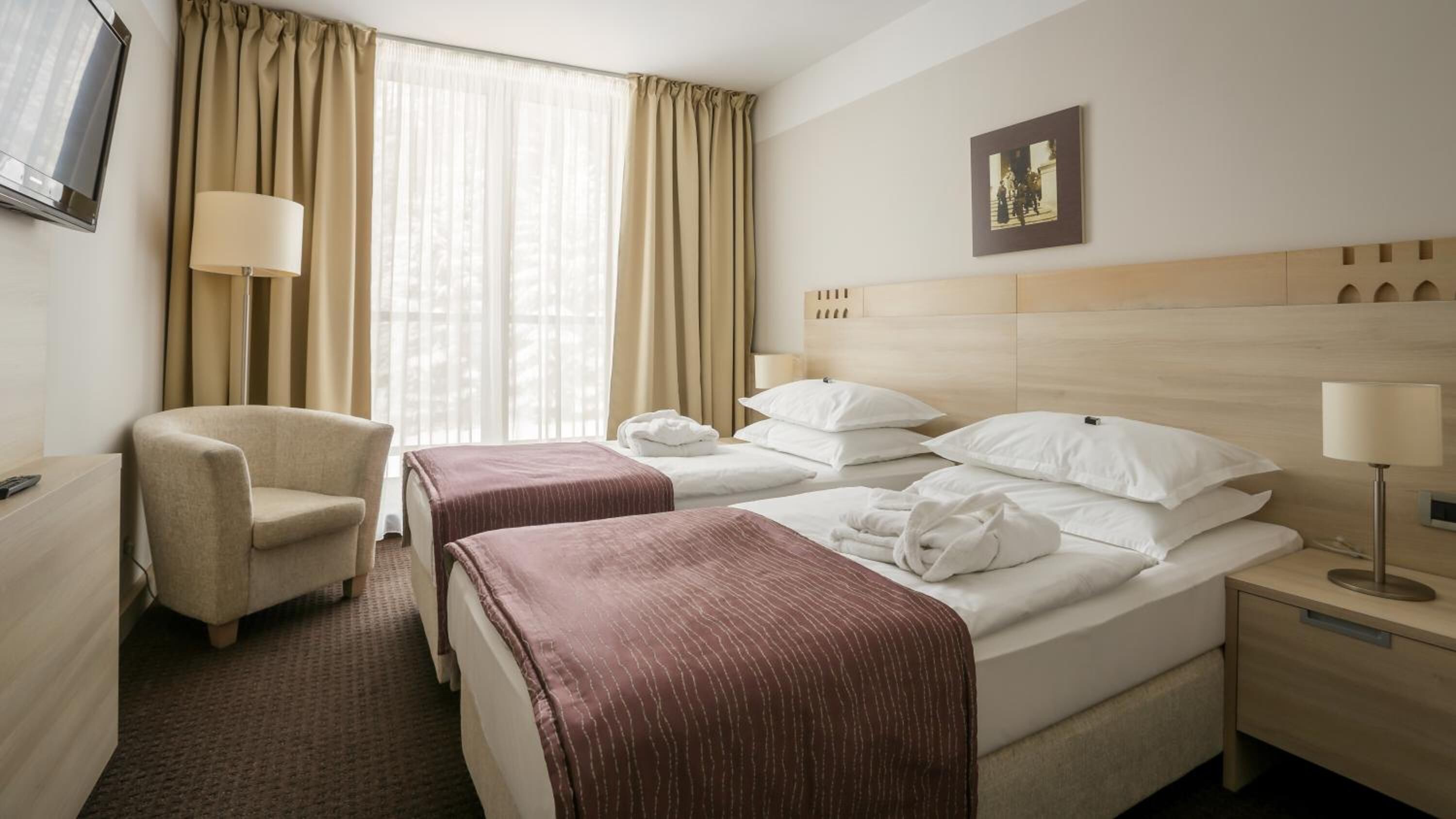 Habitación de hotel con dos camas, una silla, una mesita de noche, una lámpara y un cuadro en la pared.