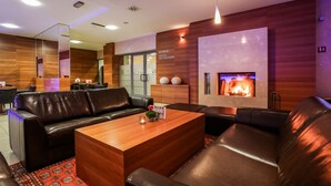 A modern lounge area with leather sofas, a wooden coffee table, and a fireplace. - Hotel Trakoscan (Bednja)