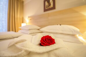 Un lit bien fait, avec du linge de lit blanc et une seule rose rouge posée sur l’oreiller.
