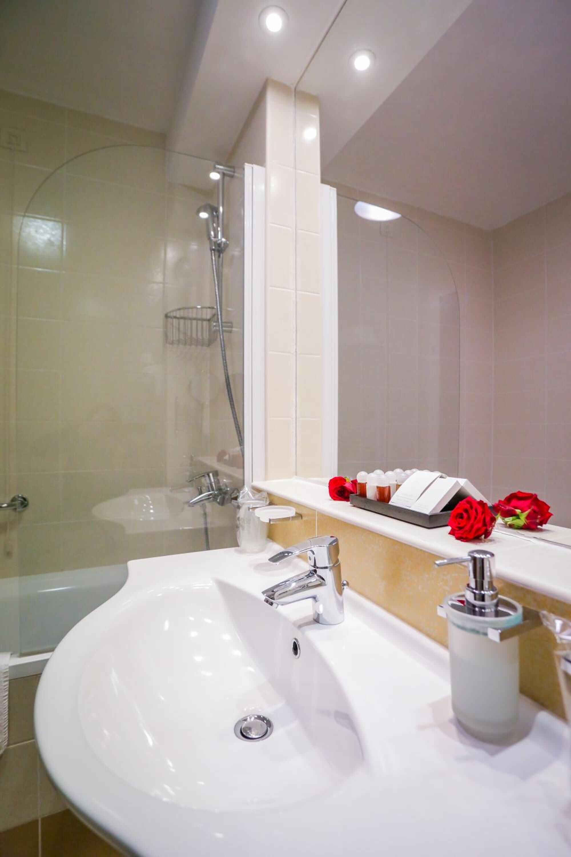 A modern bathroom with a white sink, a glass-enclosed shower, and a vanity with a mirror and a towel rack.