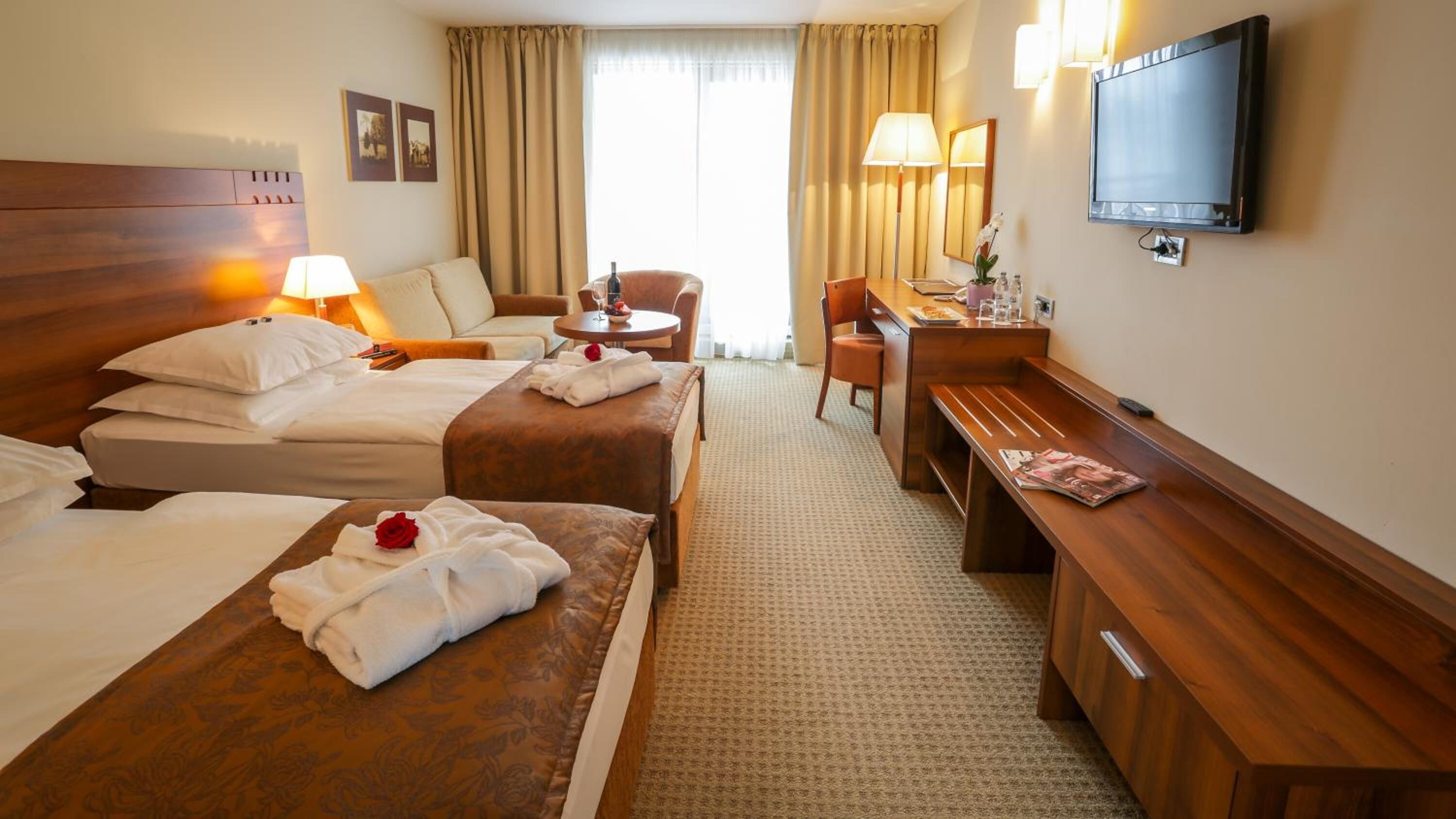 A hotel room with two beds, a desk, a chair, a TV, and a window with curtains.
