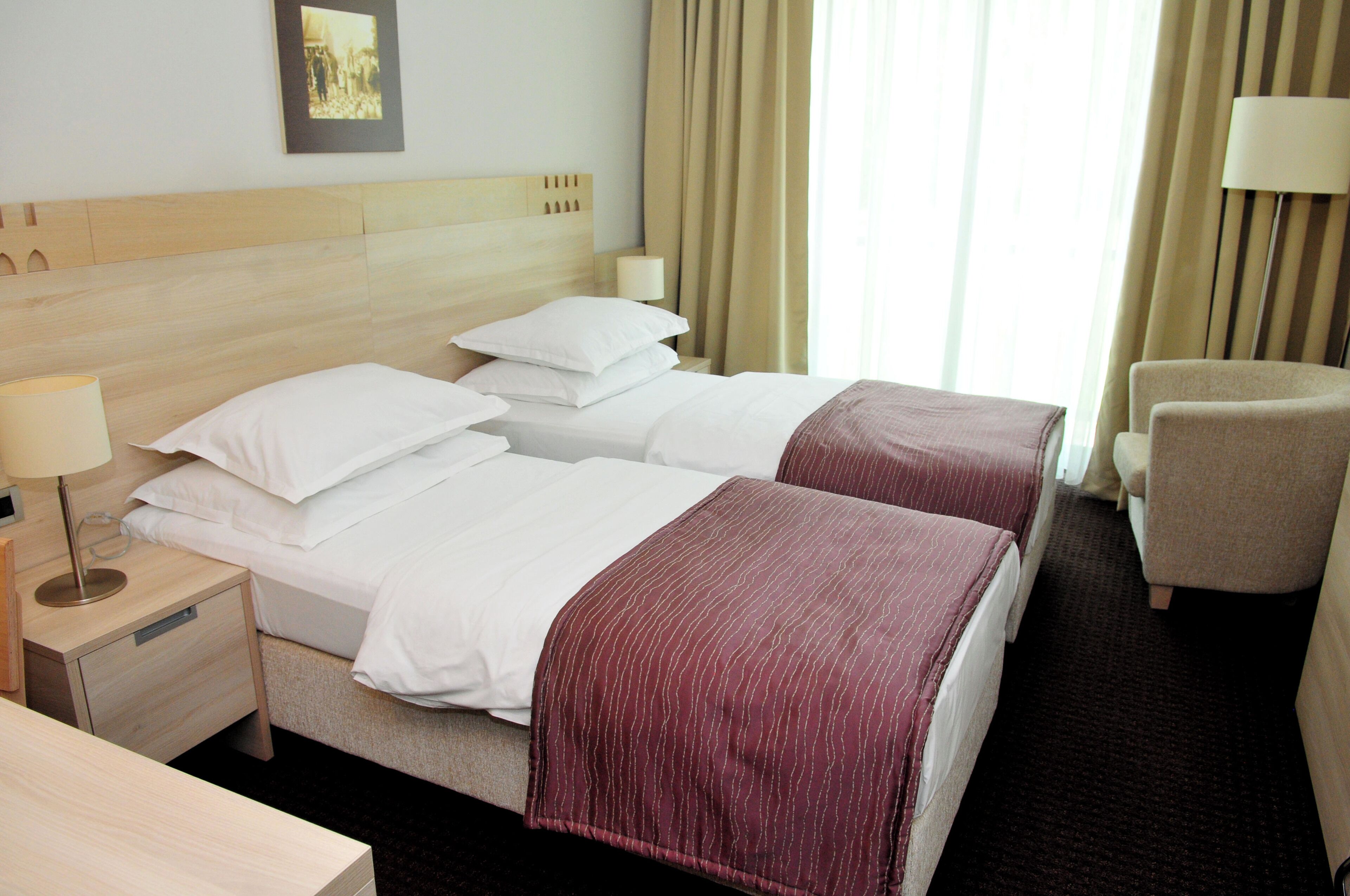 Hotellihuone, jossa on kaksi sänkyä, työpöytä, tuoli ja lamppu.