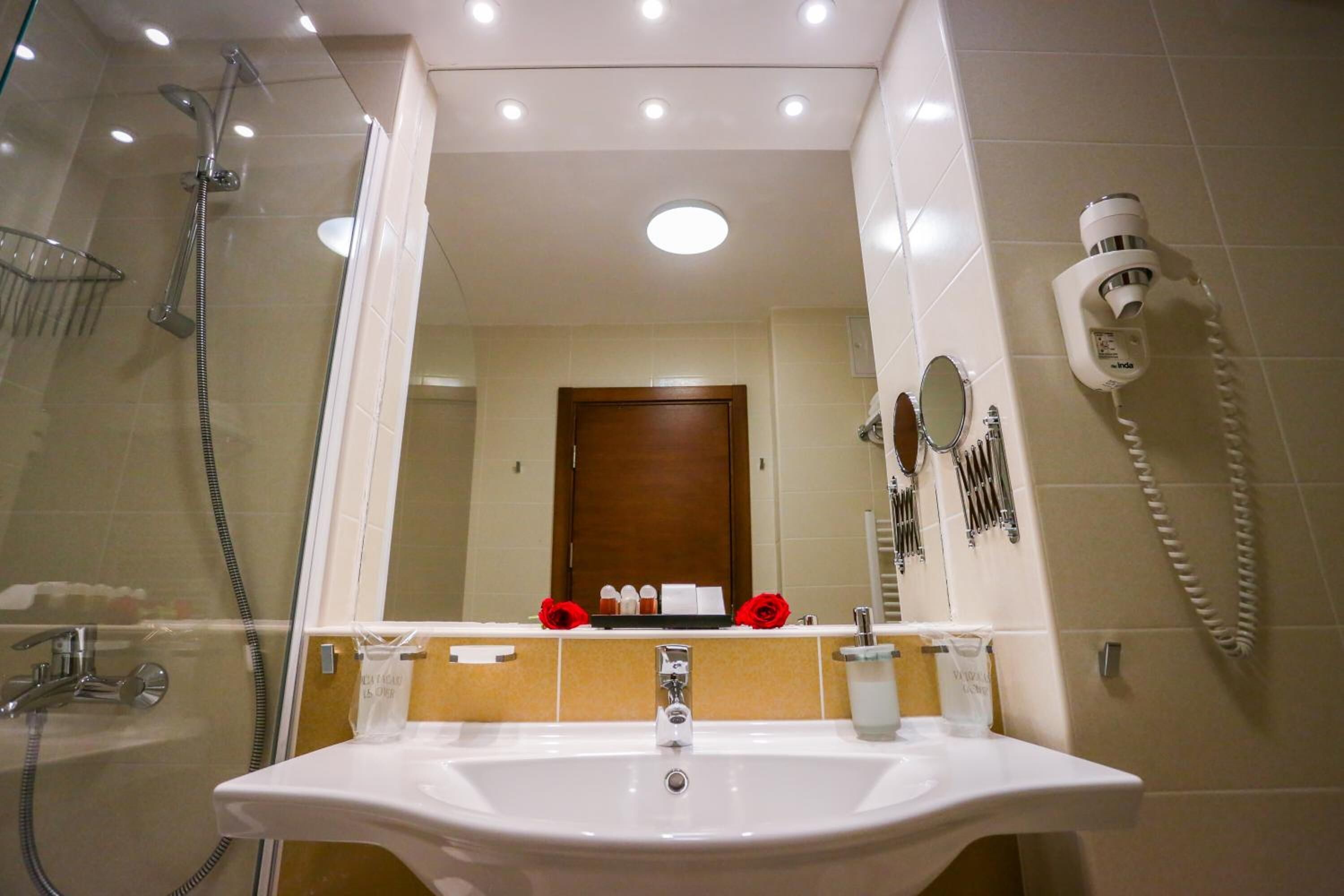 Ein Badezimmer mit einer Glaskabine zur Dusche, einem weißen Waschbecken und einem Spiegel darüber.