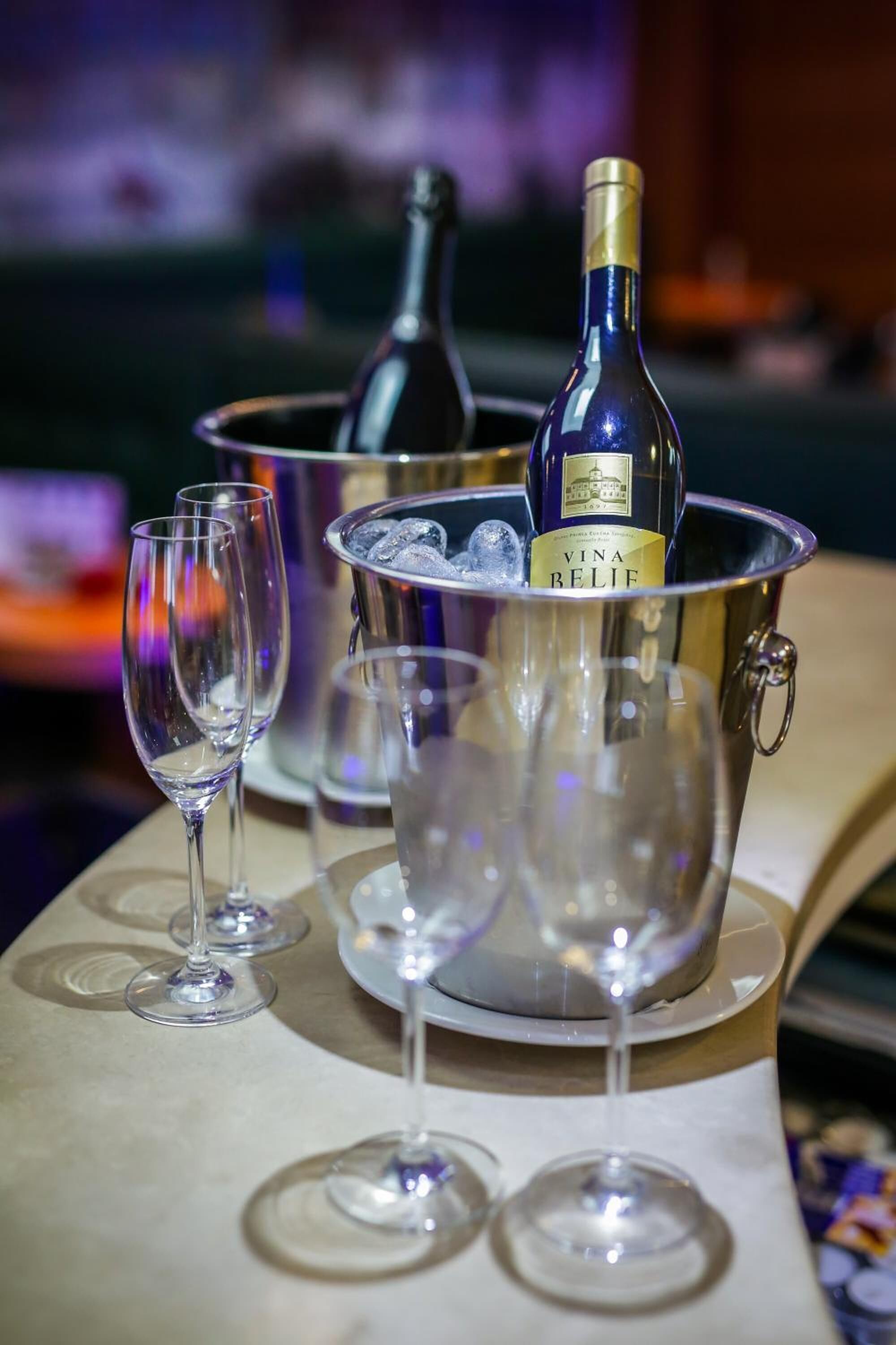 Un bar con una botella de vino Vina Belief en un balde, rodeado de copas de vino vacías.
