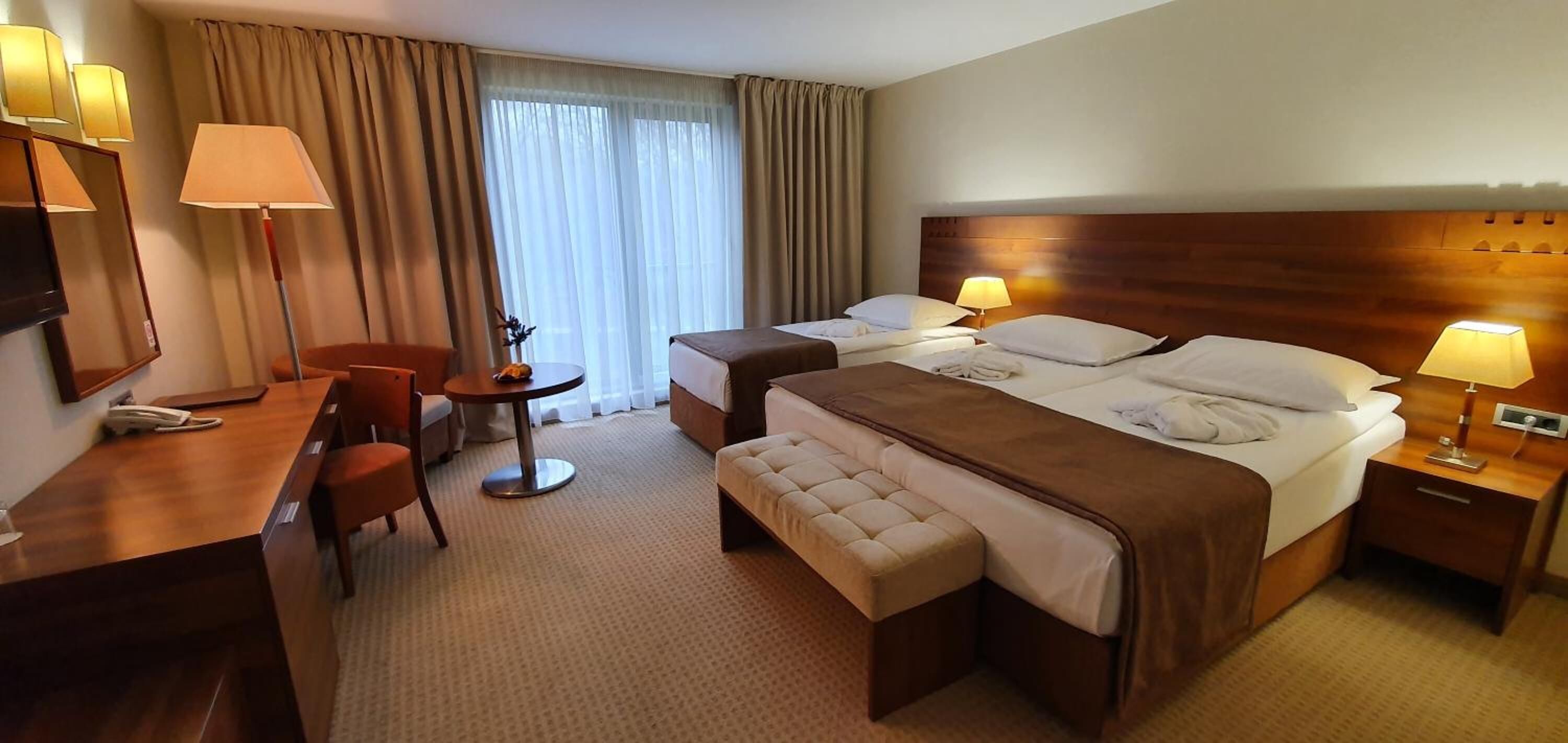Habitación de hotel con una cama grande, un escritorio con una silla, una mesita pequeña y un televisor.