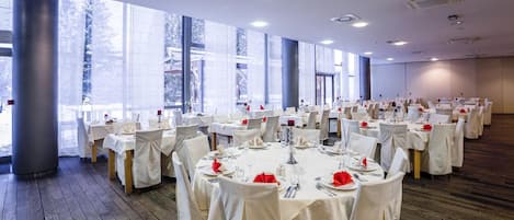 A large banquet hall with round tables set for dining, large windows, and a wooden floor.