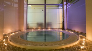 A hot tub with a tiled floor and a glass enclosure, surrounded by candles and a decorative vase. - Hotel Trakoscan (Bednja)