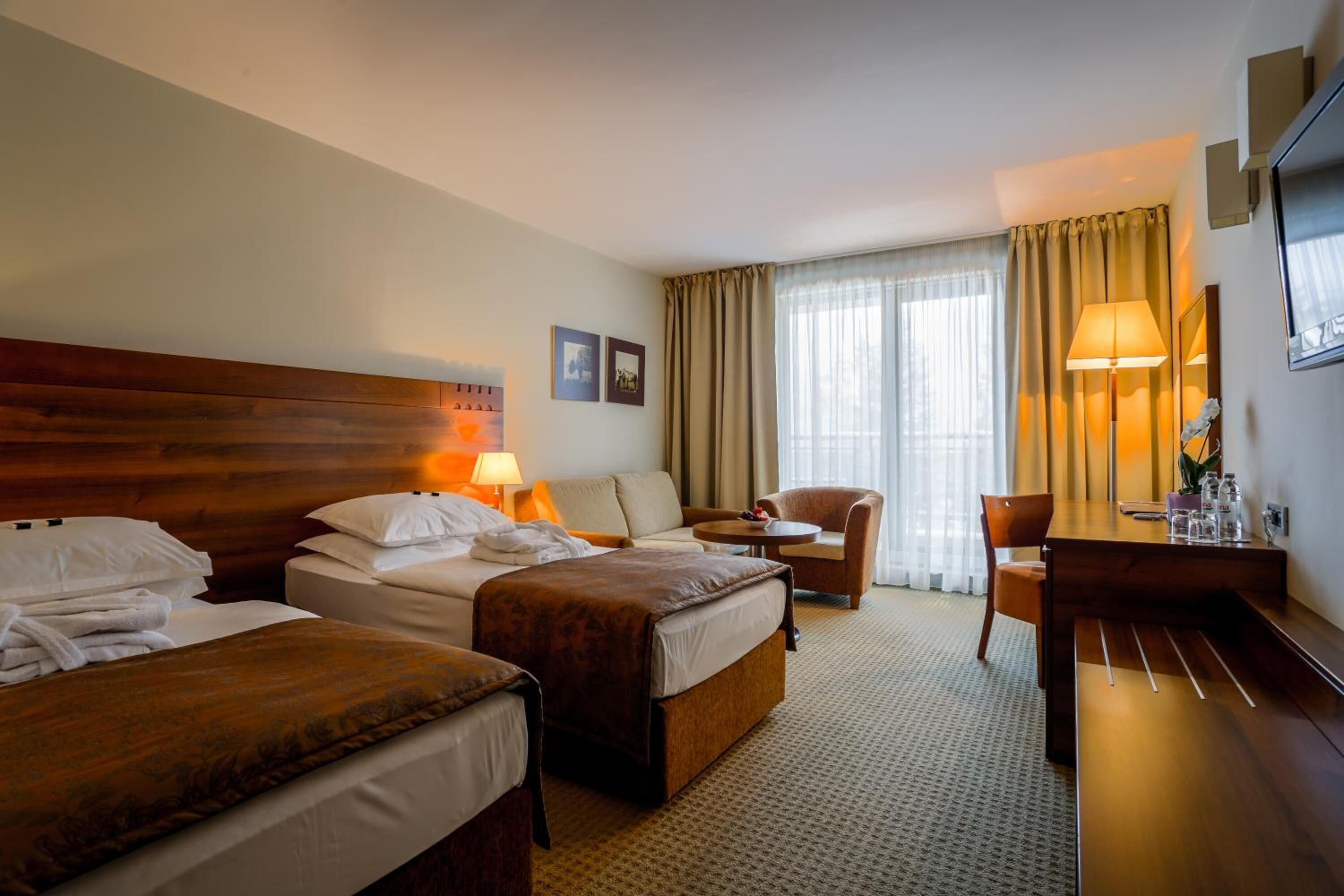 A hotel room with two beds, a desk, a chair, and a large window with curtains.