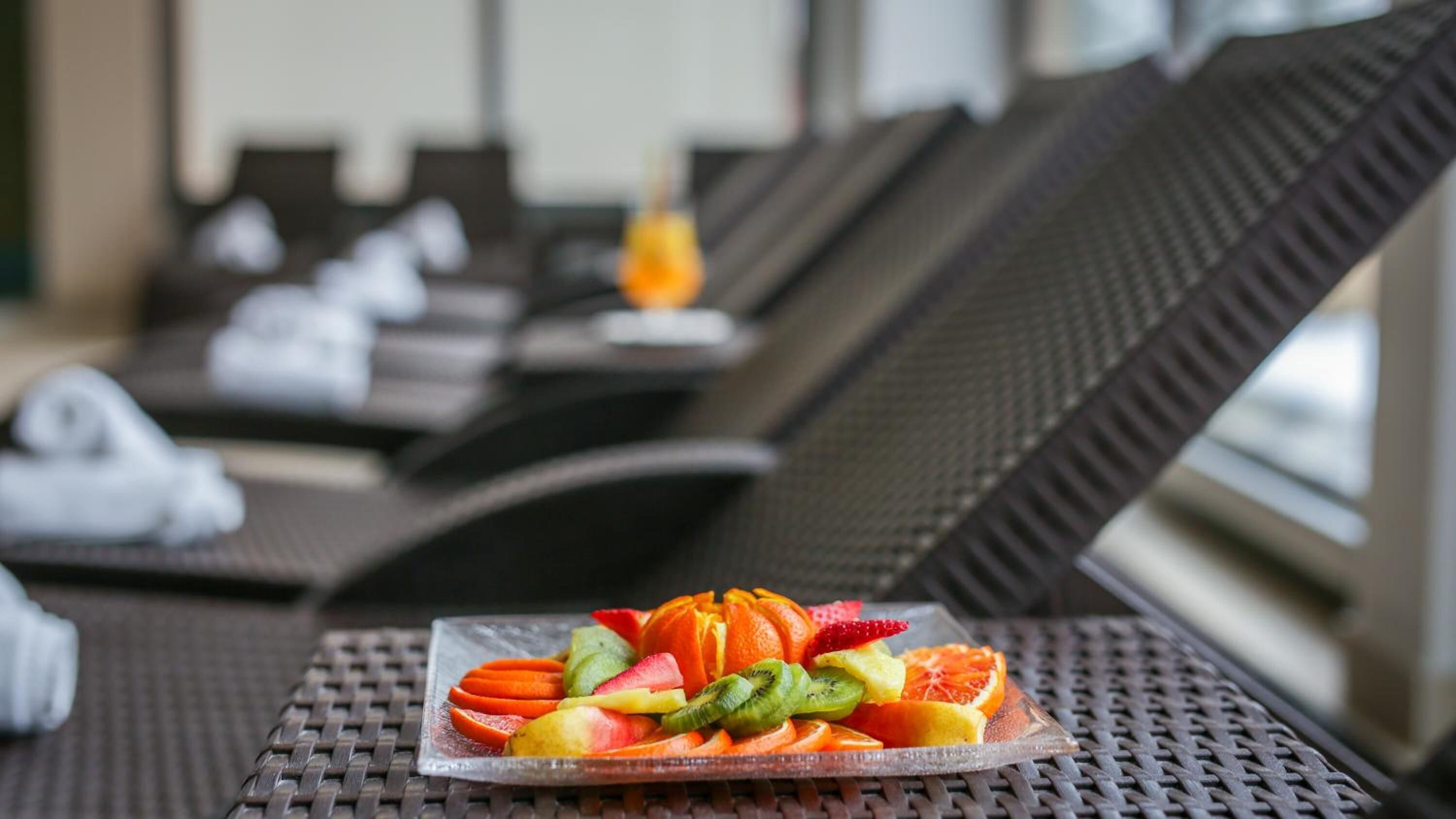 Una mesa de comedor con un plato de fruta al frente y sillones reclinables al fondo.