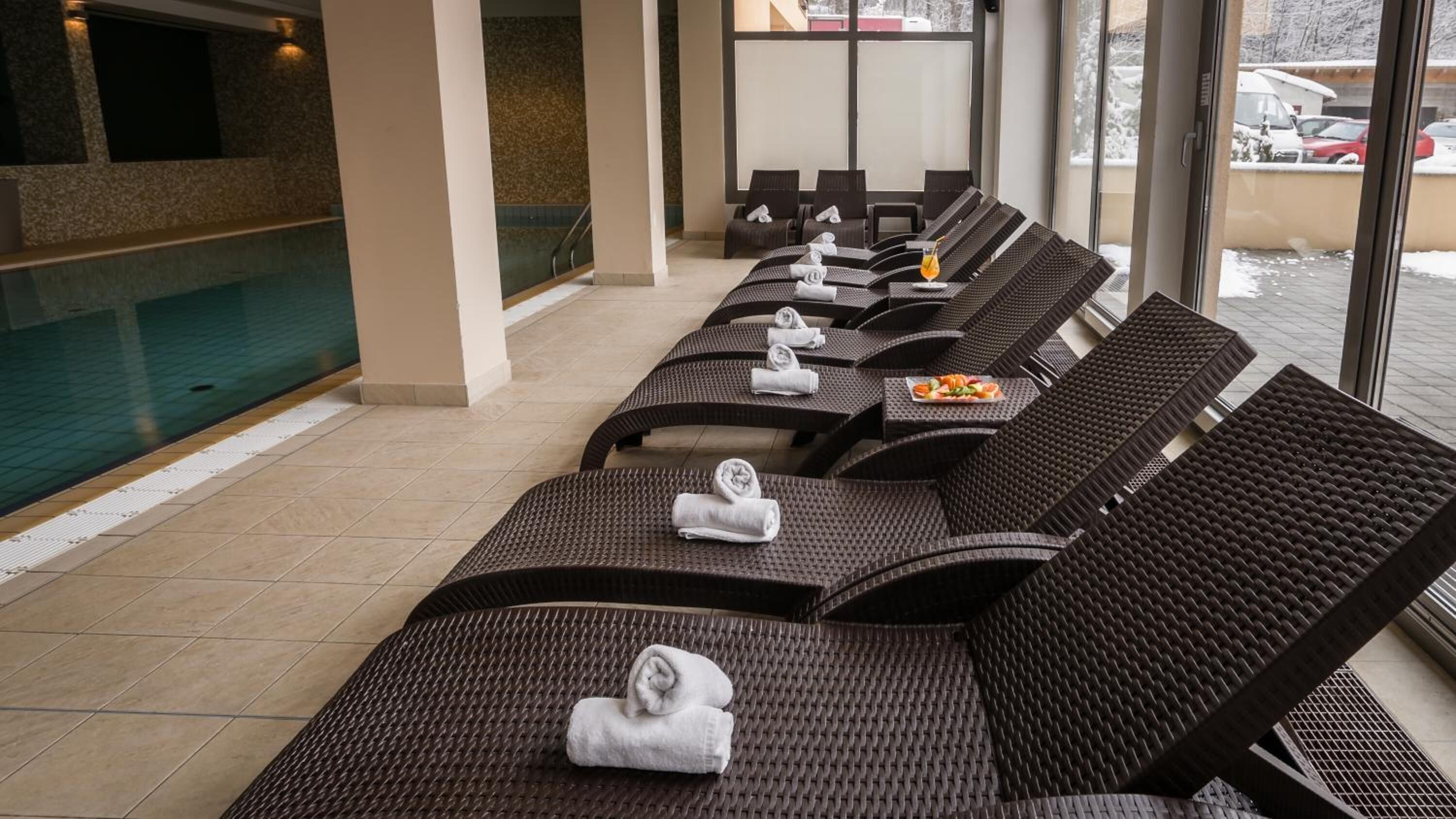 A row of sun loungers with towels, a pool, and a view of the outside.