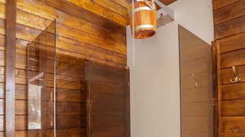 A wooden interior with a glass-enclosed shower area, a hanging copper bucket, and a white door.