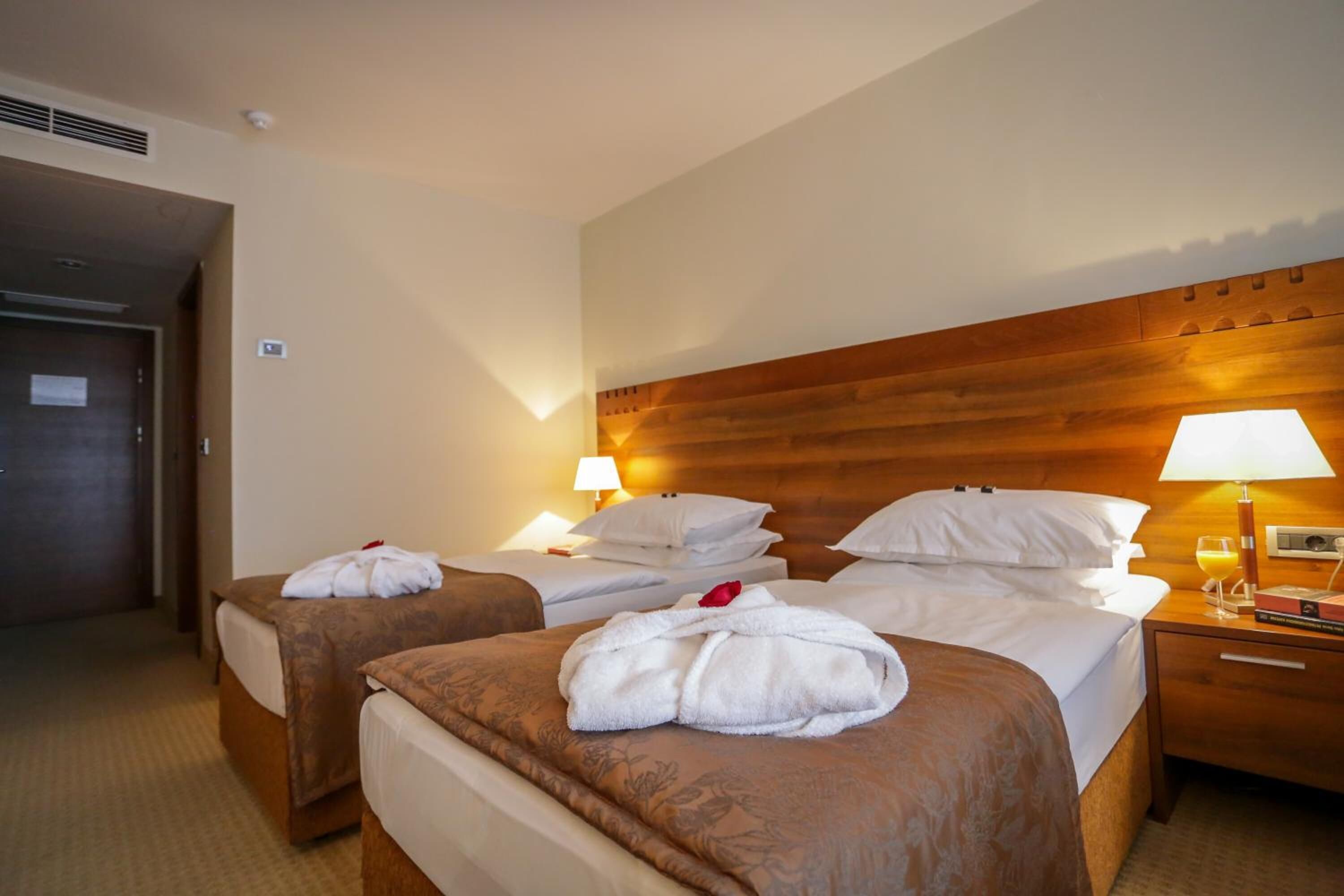 Habitación de hotel con dos camas, cada una con cabecera de madera, ropa de cama blanca y una lámpara sencilla.