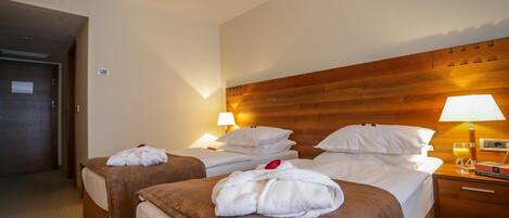 Habitación de hotel con dos camas, cada una con cabecera de madera, ropa de cama blanca y una lámpara sencilla.
