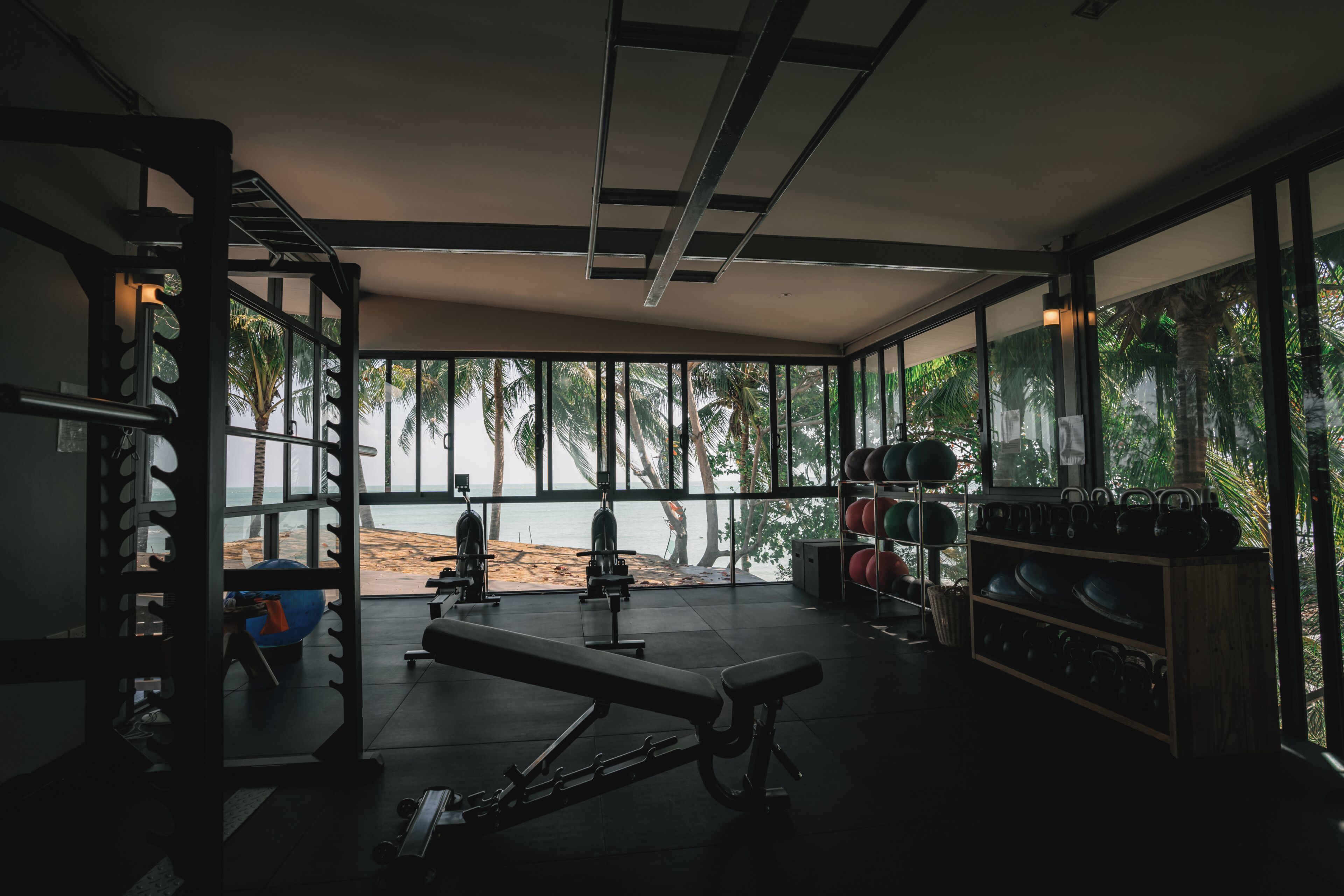 A gym with exercise equipment, a bench, and a view of the beach.