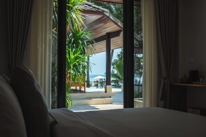 A room with a bed, a window, and a view of an outdoor area with a pool and palm trees. - Samahita Retreat Koh Samui - SHA Plus (Koh Samui)