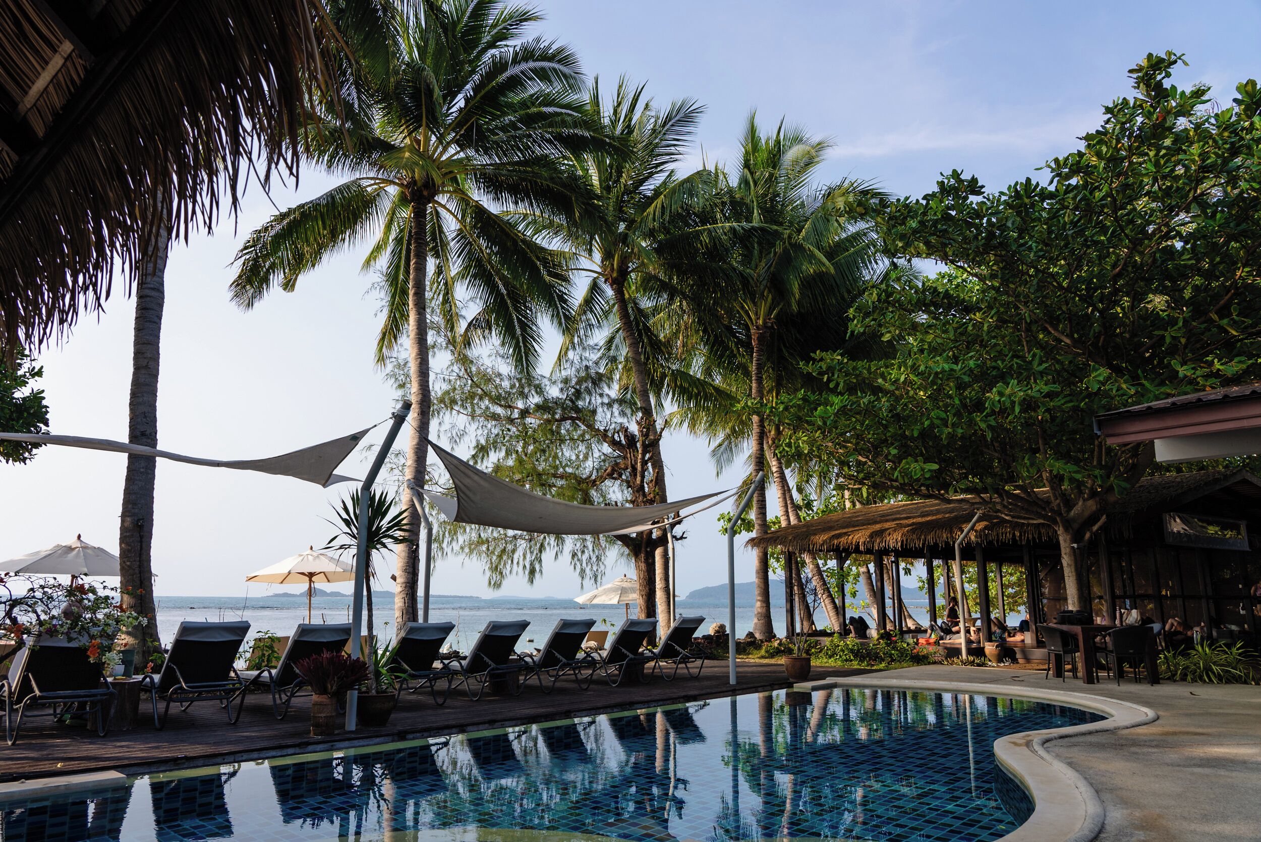 A pool area with lounge chairs, palm trees, and a view of the sea.