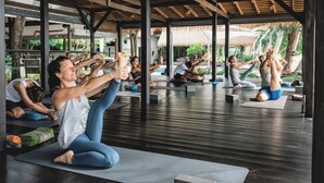 A yoga class in a covered outdoor area with wooden beams and thatched roofs, surrounded by greenery. - Samahita Retreat Koh Samui - SHA Plus (Koh Samui)