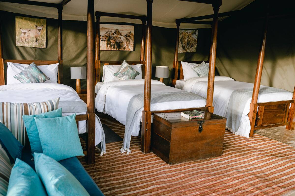 Habitación con cama con dosel y dos camas, un cofre de madera y un tapete a rayas.