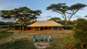Een safarilodge met een grote open tent, buitenzitplaatsen en een vuurkuil.