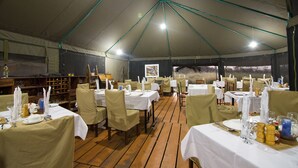 Een tentbedekte eetruimte met tafels gedekt voor maaltijden, stoelen en een houten vloer.