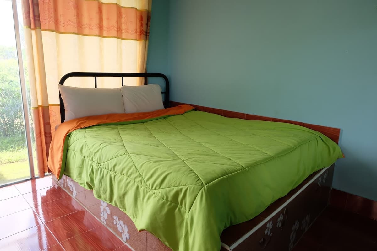 Un lit avec une couette verte, des oreillers blancs et une couverture orange.