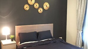 Un dormitorio con una cama de color oscuro, cabecera de madera, mesita de noche con una lámpara y un adorno en la pared.