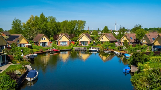 A canal with houses on one side and a wind turbine in the distance. - Europarcs IJsselmeer (Medemblik)