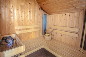 A sauna with wooden walls and benches, a bucket, and a container on the floor. - Europarcs IJsselmeer (Medemblik)
