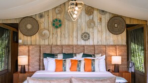 A bedroom with a wooden headboard, a bed with multiple pillows, two bedside tables with lamps, and wall decor. - Angata Ngorongoro (Ngorongoro)