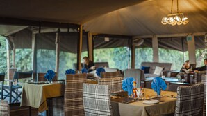 A restaurant with tables set for dining, featuring plaid chairs and blue napkins. - Angata Ngorongoro (Ngorongoro)