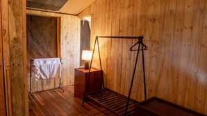 A wooden room with a wooden floor, a hanging clothes rack, a wooden bench, and a lamp on a wooden table. - Angata Ngorongoro (Ngorongoro)
