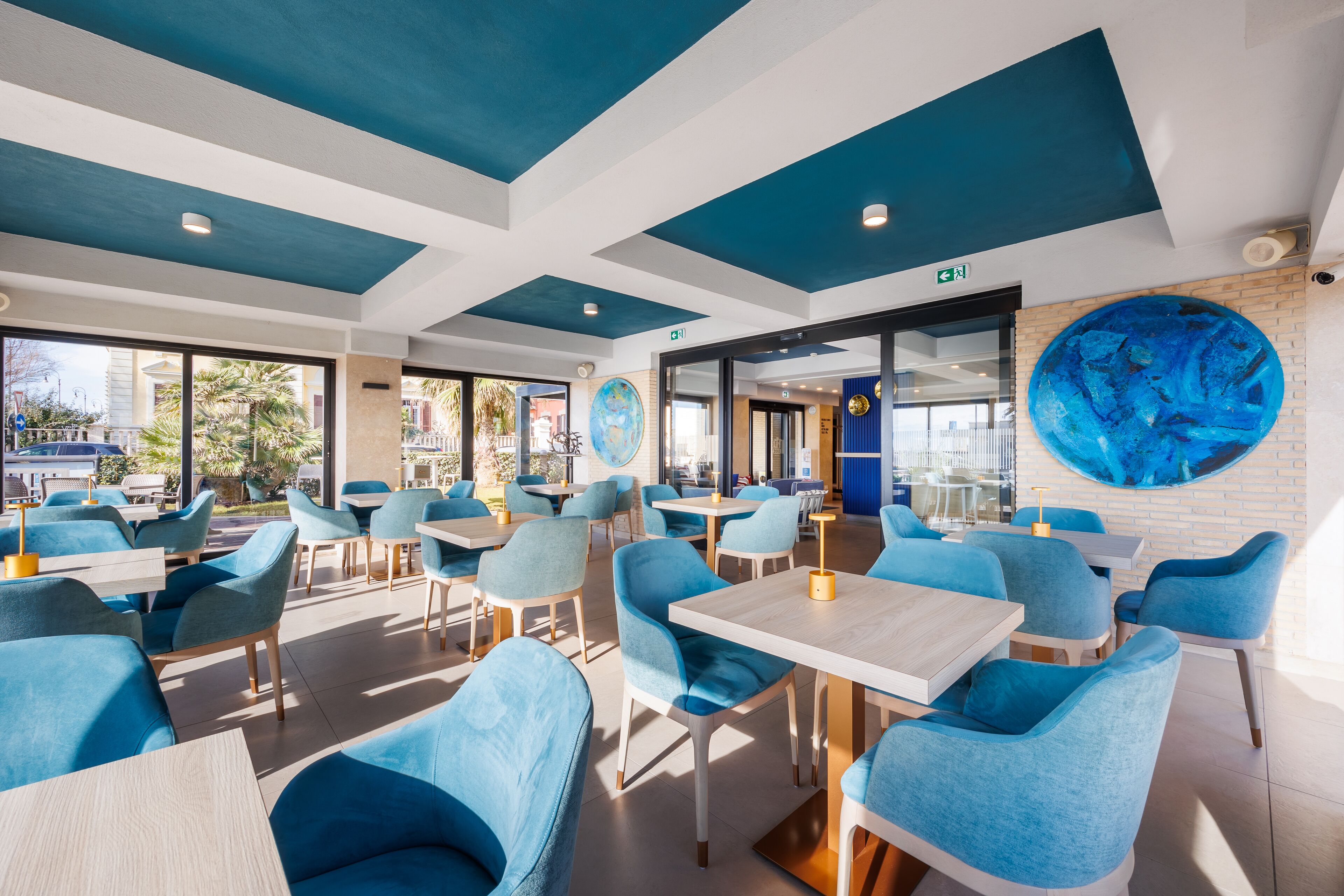 A modern restaurant with blue chairs and tables, large windows, and a blue ceiling.