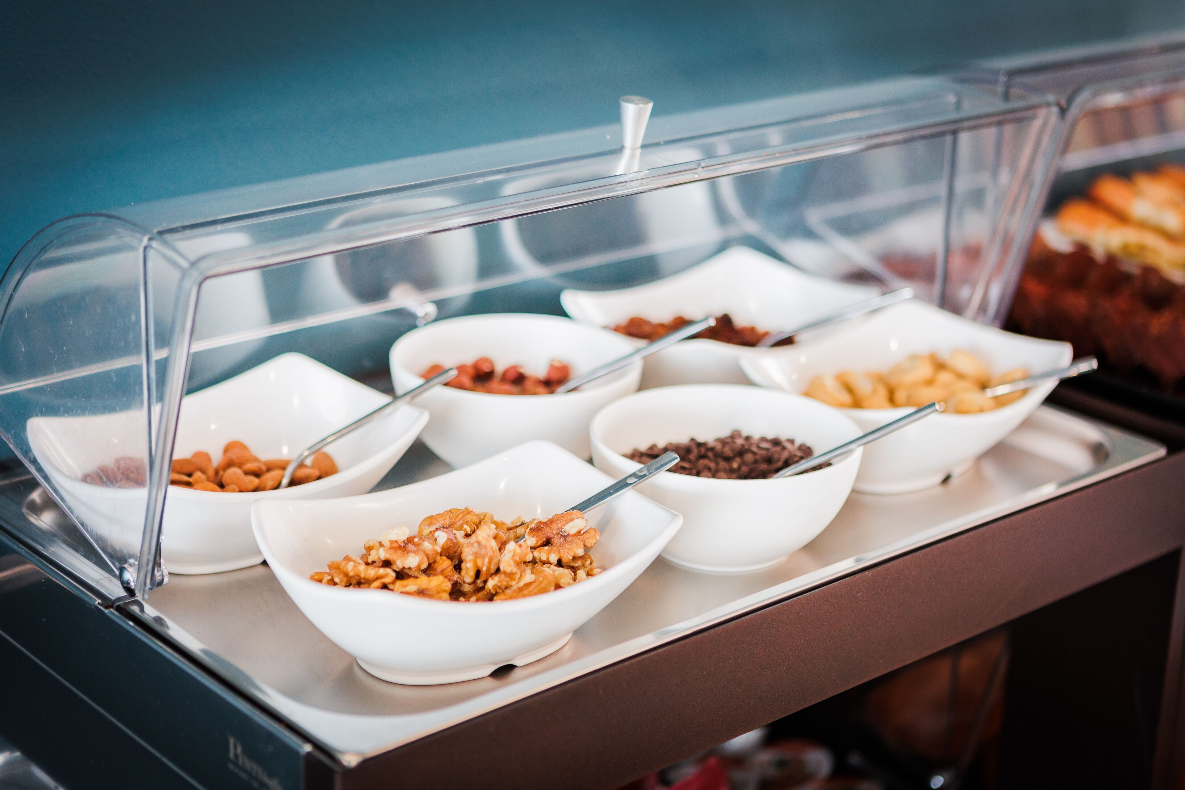 Um buffet com diversos alimentos em tigelas brancas, incluindo nozes e chocolate.
